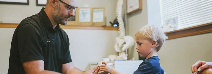 Dr. Paul Kaminski gently examines or adjusts a young child’s hand in an office environment.