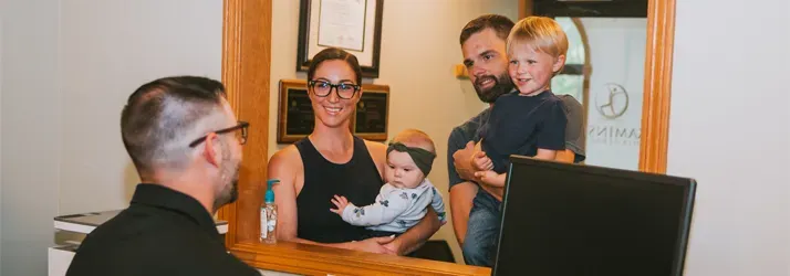 Chiropractor Grand Rapids MI Paul Kaminski Welcoming Family Group of three people interacting with a seated individual in front of a mirror, suggesting a welcoming or consultative setting.
